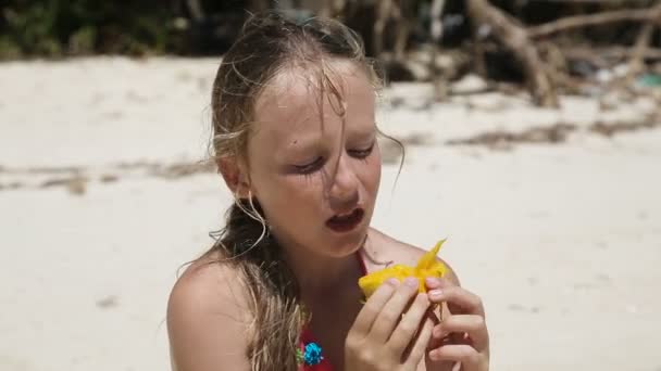 Młoda dziewczyna na plaży, jedzenie owoce mango — Wideo stockowe