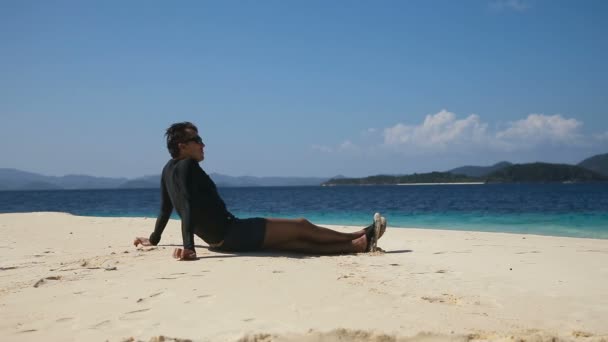 Hombre en gafas de sol sentado en la playa . — Vídeo de stock