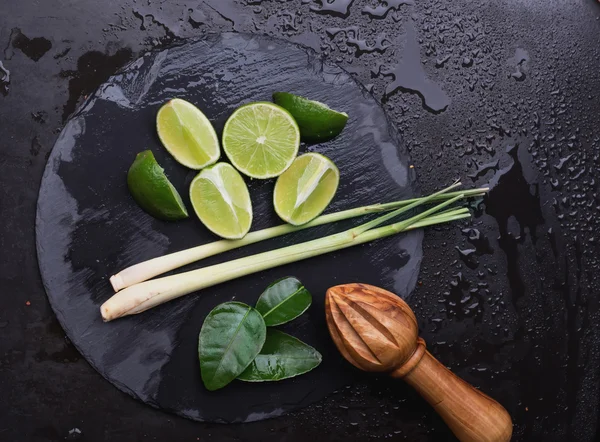 Limes, leafs and lemongrass on slate board — Stock Photo, Image