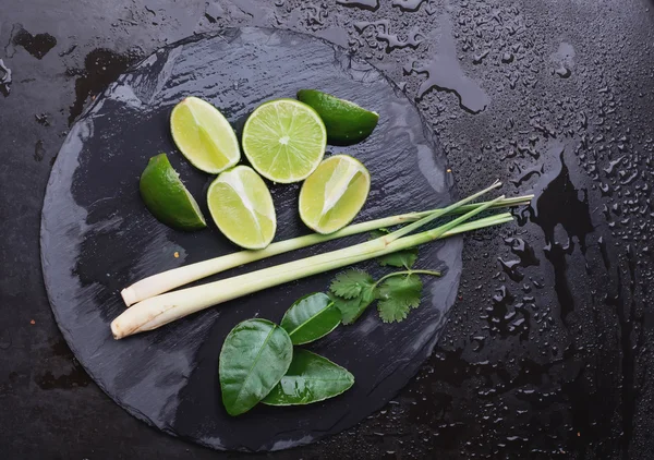 Limes, leafs and lemongrass on slate board — Stock Photo, Image