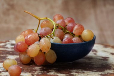 Kırsal arka planda seramik kasede bir demet pembe üzüm.