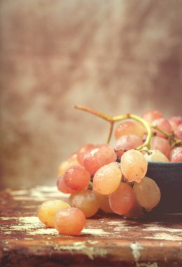 Kırsal arka planda seramik bir kasede bir demet pembe üzüm. Retro Biçimi