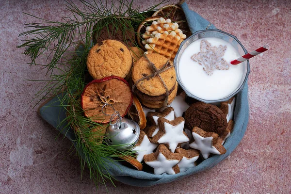 A selection of different cookies (star glazed cookies, waffles and chocolate chip cookies) in a box served with galass of milk decorated with Christmas toy and fur tree branch. Flat Lay