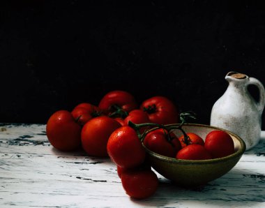 Beyaz ahşap bir arka planda seramik kavanozla kırsal seramik bir kasede dalda taze Oraganic domatesler. Temiz yeme kavramı.