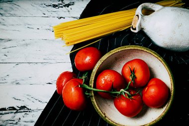 Mavi cam bir kavanozda pişirilmemiş spagetti sermik bir şişe zeytinyağı ve olgun organik domatesle birlikte arka planda peçeteyle süslenmiş. Düz Yat. Üst Görünüm