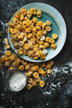Çiğ pişmemiş Cappelletti makarnası. Geleneksel İtalyan yemeği seramik tabaklar, klasik metal süzgeç ve un. Üst Manzara. Düz Yat