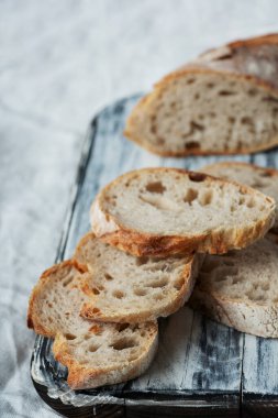 Geleneksel Fransız ekmeği baget ekmeği beyaz tahta kesim tahtasının üzerinde, masa örtüsünün üzerinde. Kırsal biçim. 