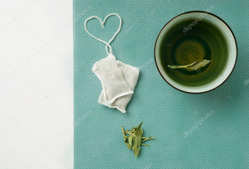 Lemon Verbena tea in  a mug and teabags with heart shaped string over a tidewater green background. Top View. Flat Lay