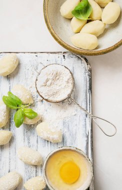 Geleneksel İtalyan patates gnocci (makarna) fesleğen yaprağı, yumurta ve unla süslenmiş. Pişmemiş makarna konsepti. Üst Manzara. Düz Yat