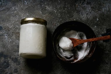 Cam kavanozda organik hindistan cevizi yağı ve Hindistan cevizi kasesinde Hindistan cevizi kaşığıyla kırsal arka planda. Sürdürülebilirlik kavramı. Üst Manzara. Düz Yat.