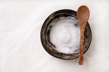 Hindistan cevizi kabında hindistan cevizi yağı ve beyaz tekstil arka planında hindistan cevizi kaşığı. Sürdürülebilirlik kavramı. Üst Manzara. Düz Yat.