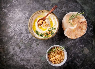 Ev yapımı humus kasesi, kaynamış nohut, otlar, pide ve zeytinyağıyla süslenmiş, rustik metal arka planda. Üst Görünüm.