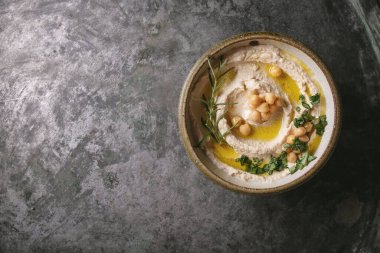 Ev yapımı humus kasesi, kaynamış nohut, otlar ve kırsal metal arka planda zeytinyağıyla süslenmiş. Üst Görünüm.
