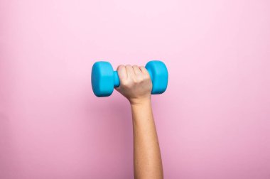 Kadının eli, pembe arka planda mavi bir dambıl tutuyor. Evde çalışma, spor ve aktivite. Kopya alanı ile spor ve sağlıklı yaşam tarzı kavramı.