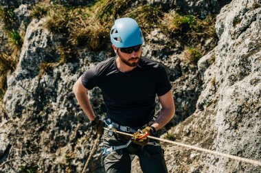 Kayalık bir uçurumdan iple inen genç bir adam sekiz figürlü ve karabinalı bir iple ipe bağlanmış. Dağlarda zorlu bir macera..