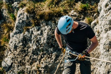 Kayalık bir uçurumdan iple inen genç bir adam sekiz figürlü ve karabinalı bir iple ipe bağlanmış. Dağlarda zorlu bir macera..