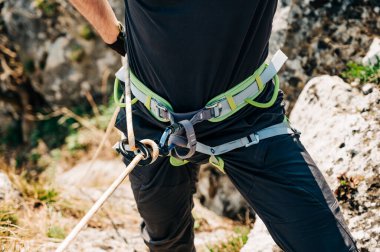 Kaya tırmanma ekipmanıyla koşumlu bir adamın açık havada iple inmeye hazırlanmasını yakın çekim. Dağ tırmanışı detayı. Tırmanma ekipmanları ve kemerinde ekipmanlarıyla tırmanıyor. Tırmanma konsepti