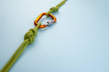 Orange Carabiner with rope. Equipment for climbing and mountaineering, alpinism, rappelling. Safety rope. Knot eight. Isolated on the blue background. Minimal concept, copy space. clipart