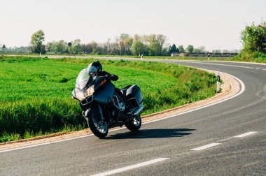 Motosiklet sürücüsü asfalt yolda tek başına gidiyor. Boş yoldaki hareketli motorcunun yaşam tarzı fotoğrafı