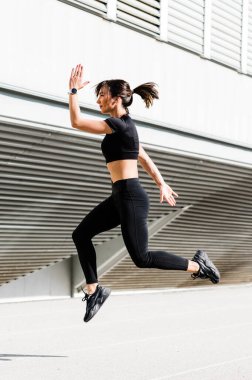 Şehir arka planında yalnız koşan bir kız. Güneşli sıcak bir günde koşu konsepti. Sağlıklı fitness yaşam tarzı. Koşucular Kulübü.