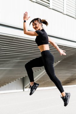 Şehir arka planında yalnız koşan bir kız. Güneşli sıcak bir günde koşu konsepti. Sağlıklı fitness yaşam tarzı. Koşucular Kulübü.