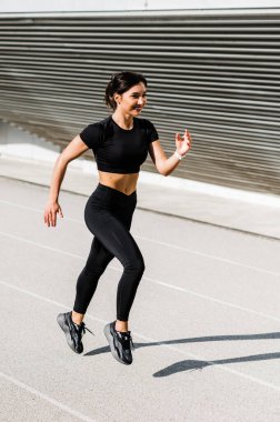 Şehir arka planında yalnız koşan bir kız. Güneşli sıcak bir günde koşu konsepti. Sağlıklı fitness yaşam tarzı. Koşucular Kulübü.