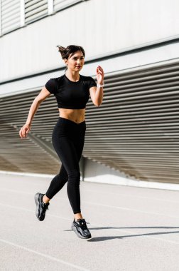 Şehir arka planında yalnız koşan bir kız. Güneşli sıcak bir günde koşu konsepti. Sağlıklı fitness yaşam tarzı. Koşucular Kulübü.