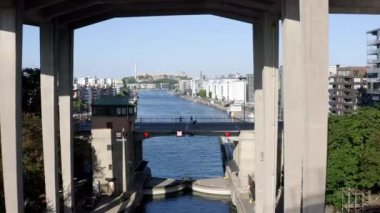 Yaz zamanı, Stockholm, İsveç. Kilitli bir köprünün altında uçan insansız hava aracı, mobiletler, insanlar, Hammarby Sjstad 'daki kanal ve körfez modern mimari, marina ve eski tekneler..