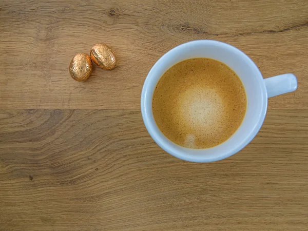 Alüminyum folyoda iki çikolatalı Paskalya yumurtası ve meşe arka planda bir kahve fincanı.