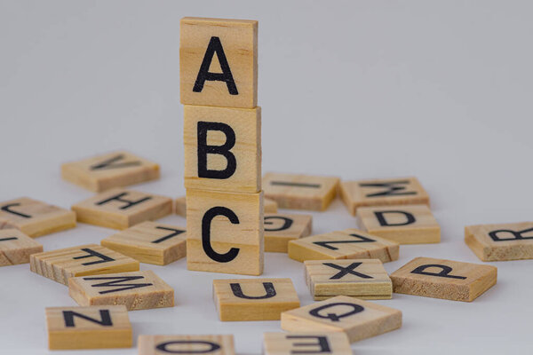 stack of square wooden blocks with the letters ABC surrounded by square wooden letters on a white background