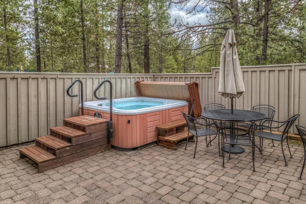 Bañera de hidromasaje en un patio pavimentador con mesa y sillas —  Fotos de Stock