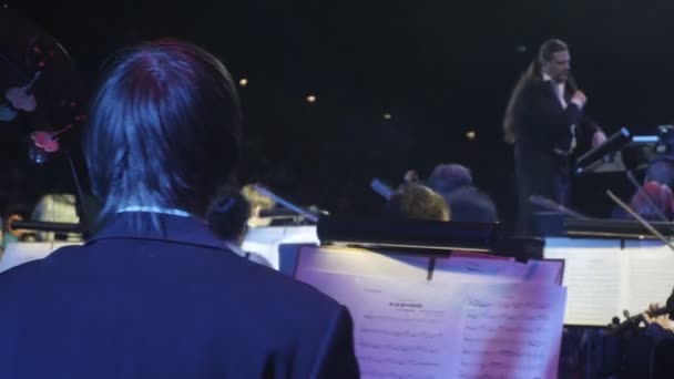 Rock Symphony toca violín y contrabajo Grandes éxitos en un concierto en Kiev Director de orquesta Libros de música en el escritorio Director Nikolai Lysenko — Vídeo de stock