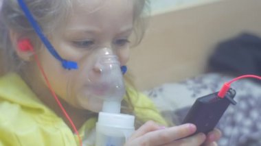 Kız Inhaler ile oynarken ile akıllı telefon dinleme sarı bluz ile başlıklı bir Smartphone çocuk ile kulaklık müzik bir hastanede oturuyor olduğunu