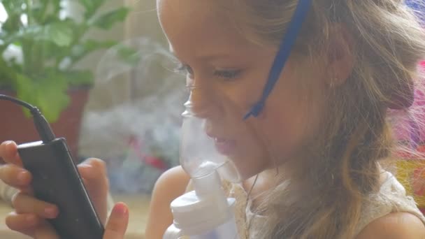 Девочка закрывает лицо ребенок дышит Nebulizer ингалятор играет с мобильного телефона сидя с маской Nebulizer на лице держа мобильный телефон пара — стоковое видео