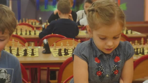 Blond flicka med flätor örhängen spelar schack styrelser på en tabell barn spelar schack på schack konkurrens för förskolebarn i Opole Polen — Stockvideo