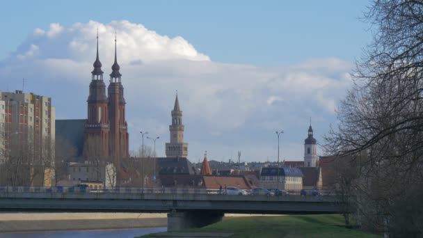 Pessoas em uma ponte Dois Spires Red-Blocked Torres de Catedral Cidade Velha Edifícios Modernos Ponte Rio Carros Ônibus são conduzidos por uma ponte Cityscape Nublado — Vídeo de Stock