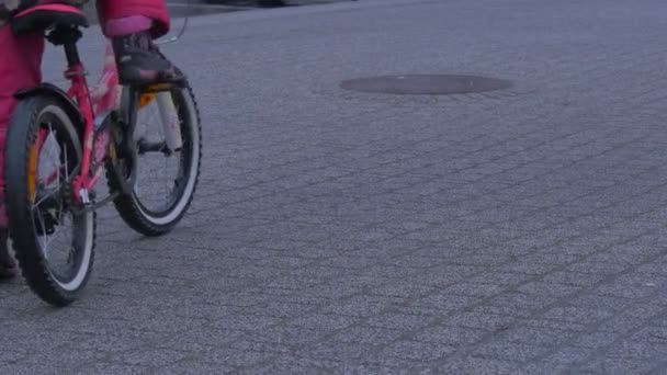 Kinderbeine aus nächster Nähe Kind sitzt auf Fahrrad rosa Hose fängt an Rad zu fahren Kleines Mädchen fährt Fahrrad auf zwei Rädern durch eine Stadt an einer Straße — Stockvideo