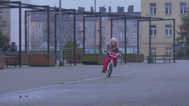Kid rijdt een fiets snel in de richting van een camera geasfalteerde plaats sport grond klein meisje rijdt een tweewielige fiets Wheeling in een stad door een straat — Stockvideo