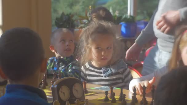 I bambini stanno aspettando una partita alle scacchiere Ragazzi e ragazze stanno giocando a scacchi al torneo di scacchi per bambini in età prescolare Sole splende attraverso la finestra — Video Stock