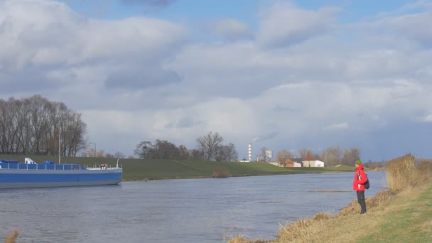 Hombre turista está caminando en la orilla del río mochilero está parado en el pequeño río azul barco en un río sol brilla a través de nubes flotante gris cúmulo — Vídeos de Stock