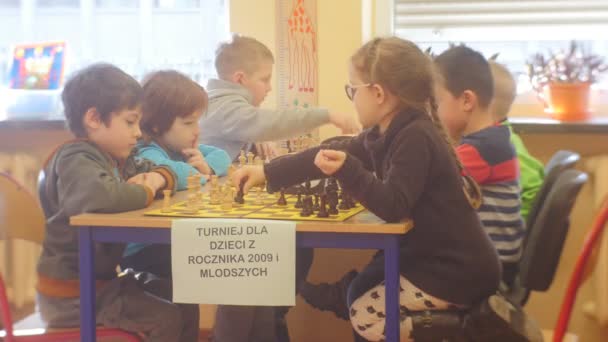 Dzieci siedzą w szachy deski przenieść napis kawałki w Polscy chłopcy i dziewczyny grają szachowy Turniej Szachowy dla przedszkolaków — Wideo stockowe