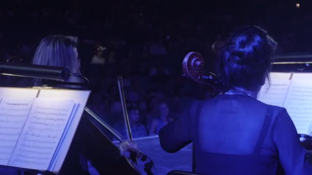 Kvinnor är spela cello med en båge Rhythmically musikböcker är montern Greatest Hits av Rock symfoni konsert i Kiev ledare Nikolai Lysenko — Stockvideo