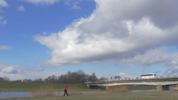 Турист идет на поле освещения с солнечным мостом автомобили Лорри приводятся в движение автомобильным мостом через Малую реку Белый кучевой голубой небо зеленые луга — стоковое видео