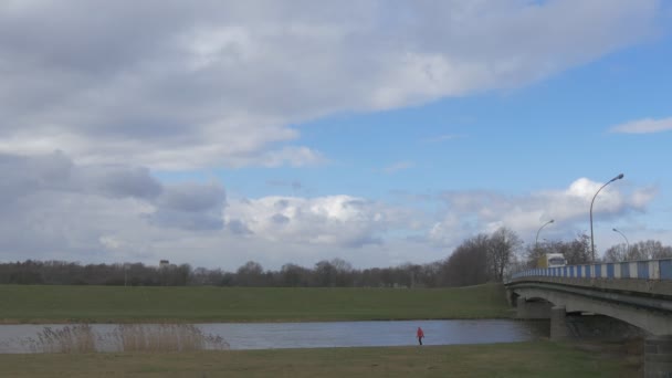 De mens is wandelen langs rivier auto brug auto's vrachtwagens worden gedreven door een auto Bridge via kleine rivier wit Cumulus zweven door Blue Sky groene weiden — Stockvideo