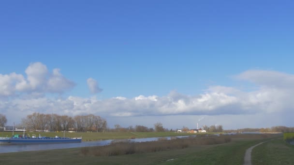 Barco azul está estacionado a la orilla del río Día soleado Ramas desnudas Árboles Nubes blancas en un cielo azul claro Edificios en un horizonte Seco Caña Verde Hierba — Vídeos de Stock