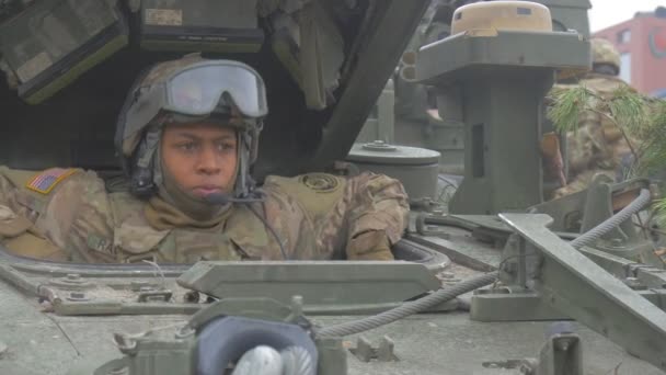Operatie van de NAVO opleiding Polen Afro-Amerikaanse soldaat in helm zit in Tank cabine praten via microfoon lachend groen Pine tak op een Tank — Stockvideo