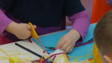 Opole çocuk aile usta-sınıfı bir iplik makas ile tutkal için bir mavi Kağıt Kids Are yapmak için bir gökkuşağı-aplike oturmuş masada işler keser