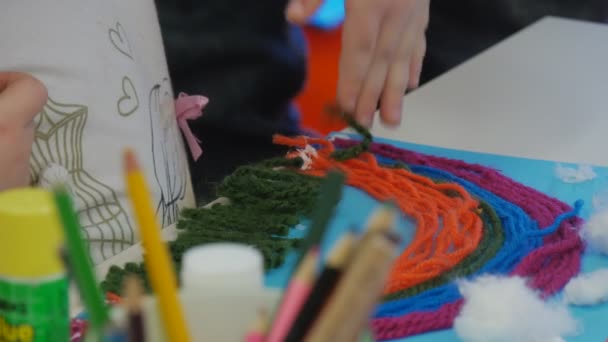 As mãos de criança estão cortando uma tesoura de rosca verde fazendo uma grama para fios-Applique Rainbow-Applique de fios coloridos sentados na mesa na sala de aula — Vídeo de Stock