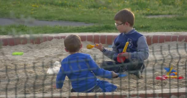 Twee jongens in de Sandbox graven een gat en gooien zand speelgoed schoppen — Stockvideo