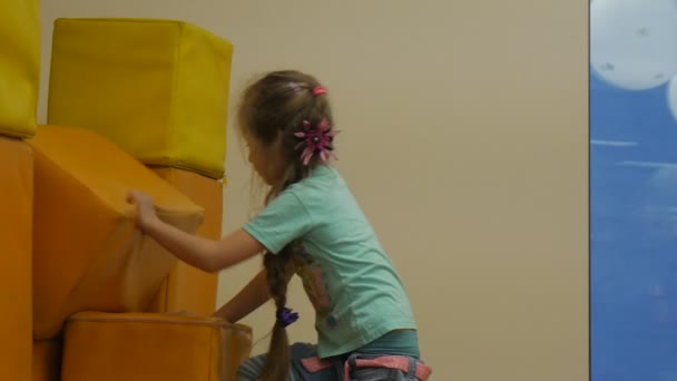 Kid is Climbing to a Yellow Mats Building a Wall Put One Mat the Other Brincando com tapetes Sorrindo em forma de cubo Travesseiros Pequena Loira Menina Brincando Quarto — Vídeo de Stock